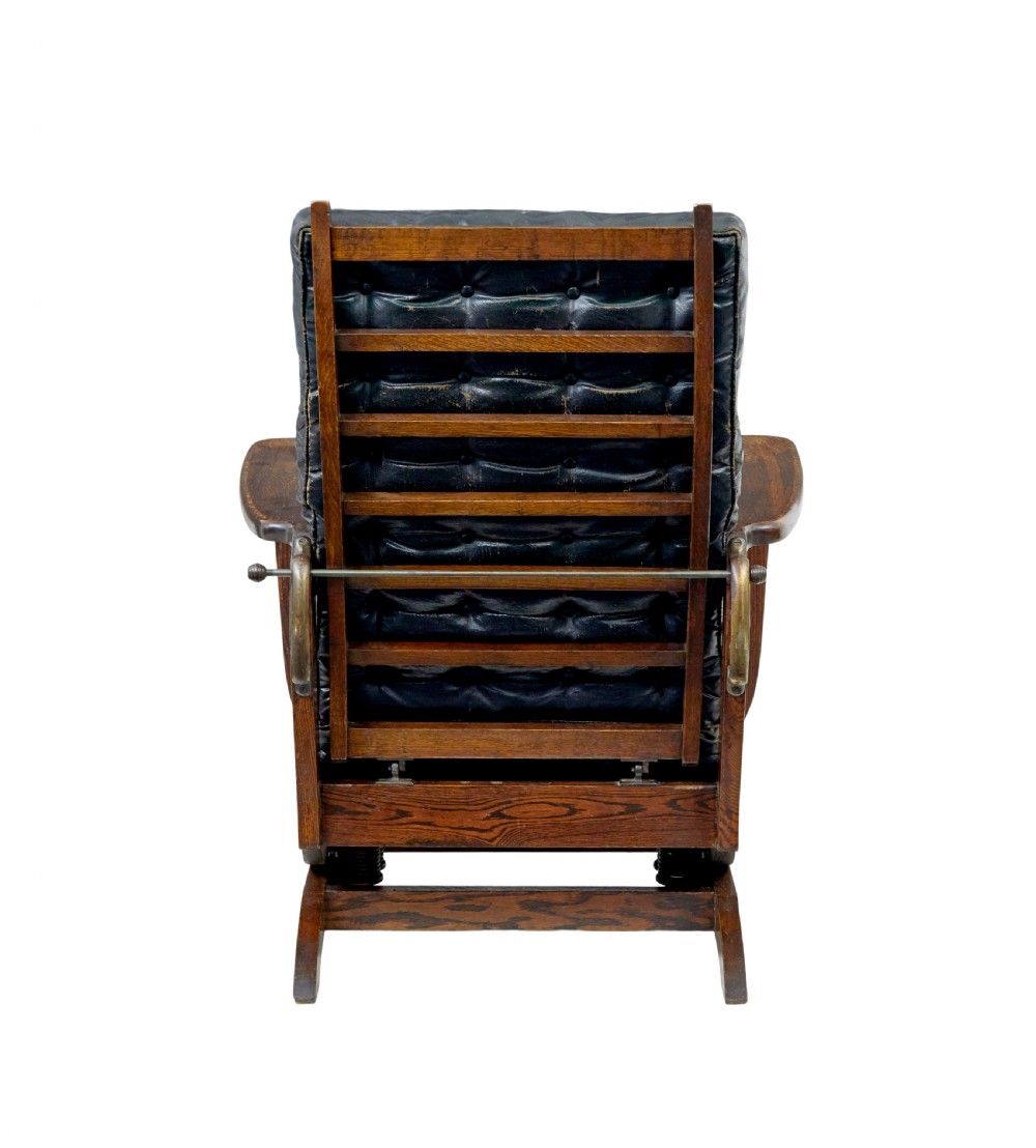 An early 20th-century dark oak platform rocking chair featuring button-tufted black leather cushions and carved front feet. View VI