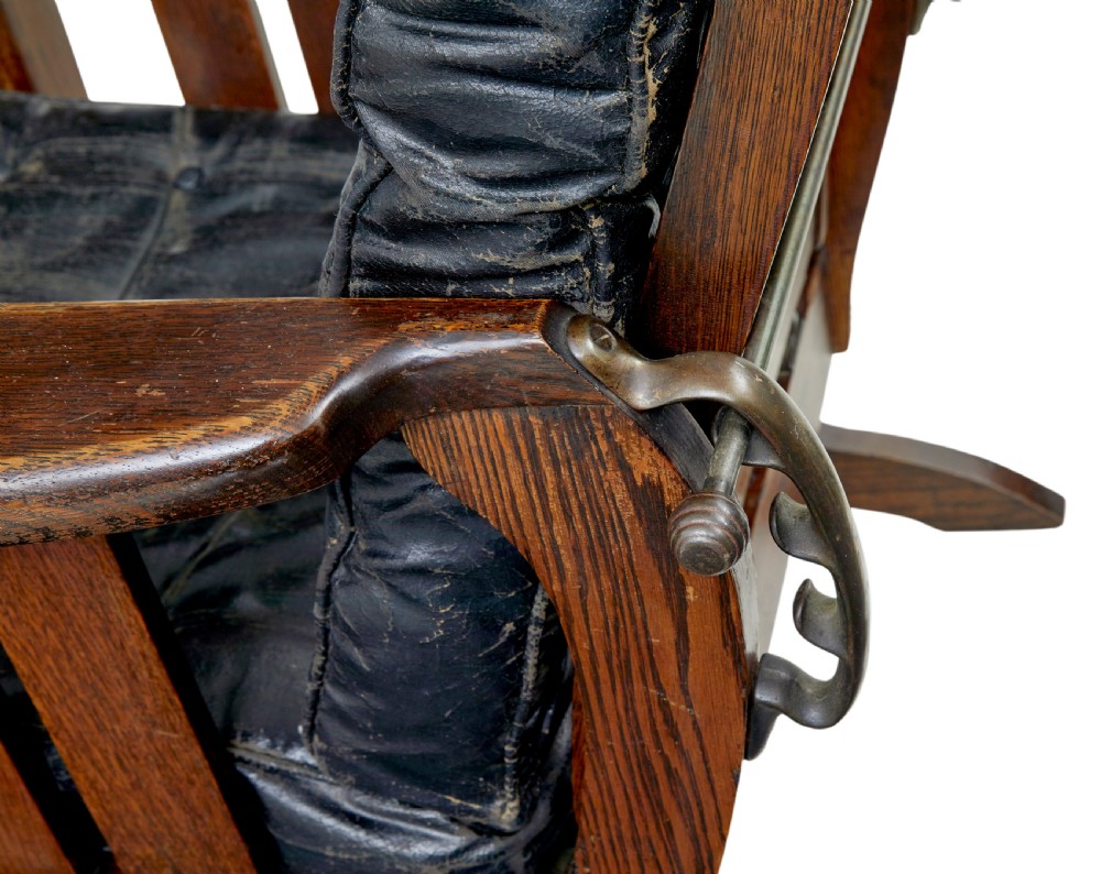 An early 20th-century dark oak platform rocking chair featuring button-tufted black leather cushions and carved front feet. View VII