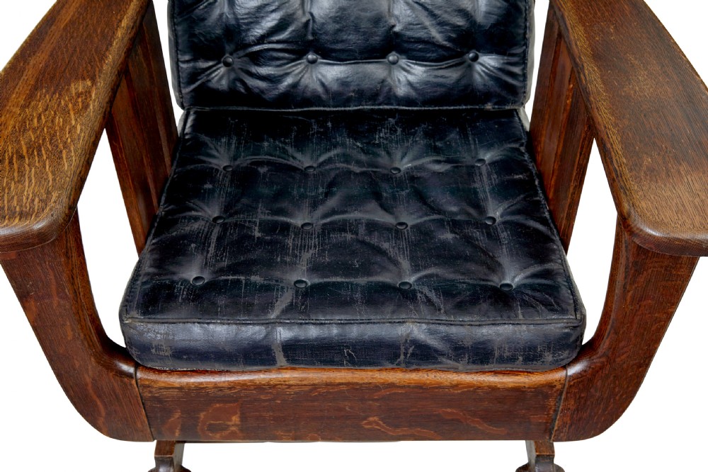 An early 20th-century dark oak platform rocking chair featuring button-tufted black leather cushions and carved front feet. View X