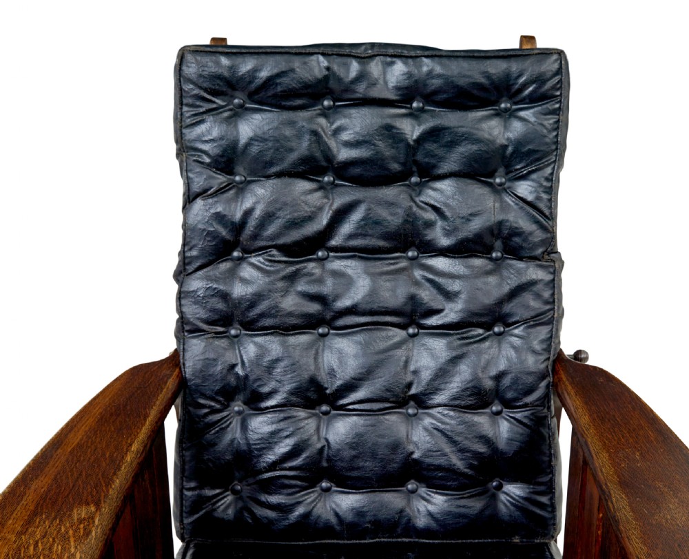 An early 20th-century dark oak platform rocking chair featuring button-tufted black leather cushions and carved front feet. View XI