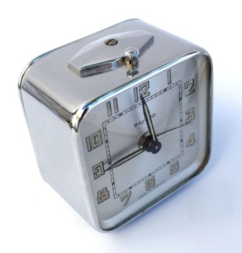 fig 1. A square French Art Deco chrome alarm clock with stylized yellow numerals, a silver dial, and a top shut-off button.