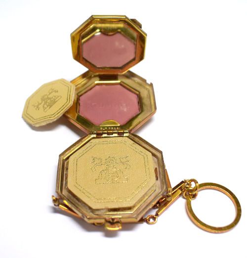 fig 1. An octagonal Art Deco gold-tone metal compact featuring a green enamel top with a central black floral motif and an attached finger ring chain.