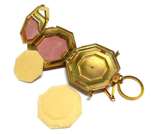 fig 2. An octagonal Art Deco gold-tone metal compact featuring a green enamel top with a central black floral motif and an attached finger ring chain.