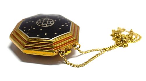 fig 1. An octagonal Art Deco powder compact by Richard Hudnut featuring black enamel, a central geometric motif, gold-tone trim, and an attached chain.