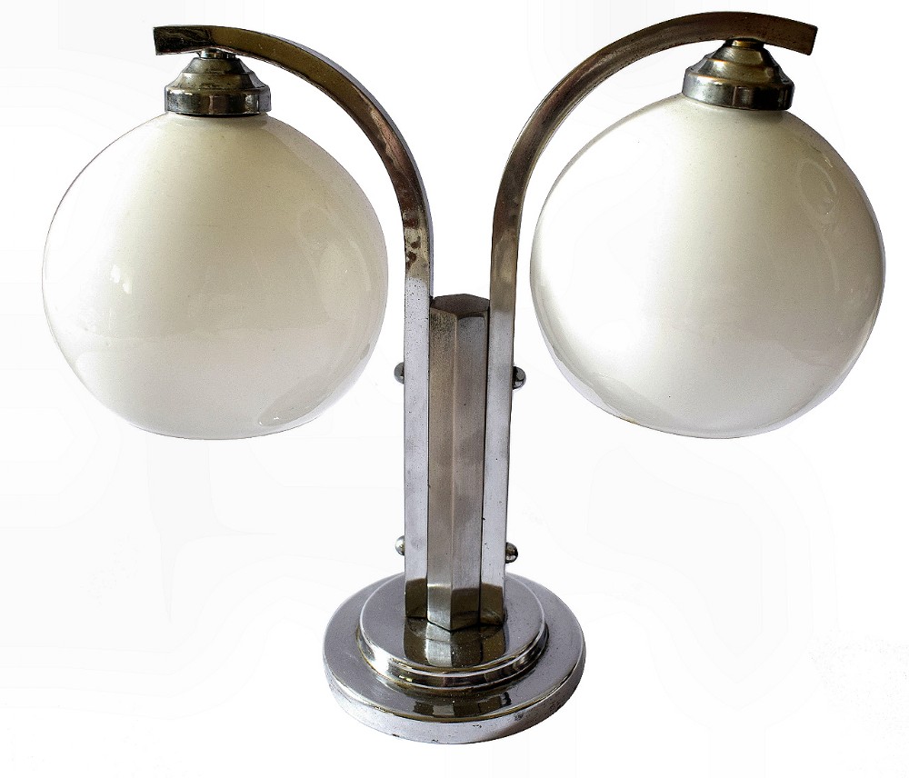 An Art Deco double table lamp featuring a chrome-plated stepped base, twin curved arms, and two white spherical glass shades.