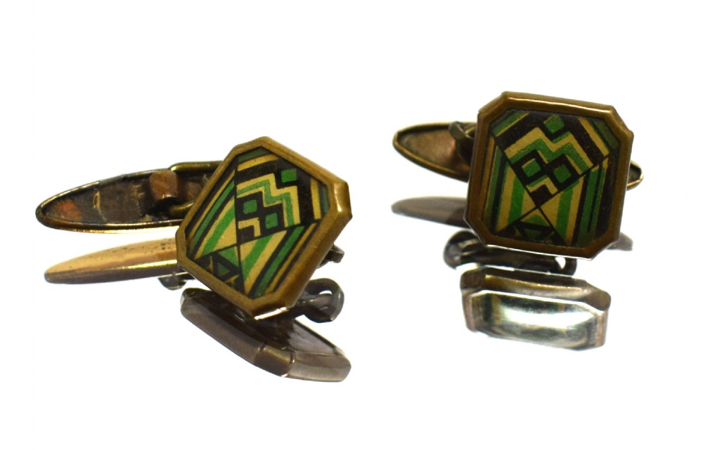 A pair of Art Deco gents cufflinks featuring octagonal faces inlaid with geometric green, black, and yellow enamel patterns framed in brass metal.