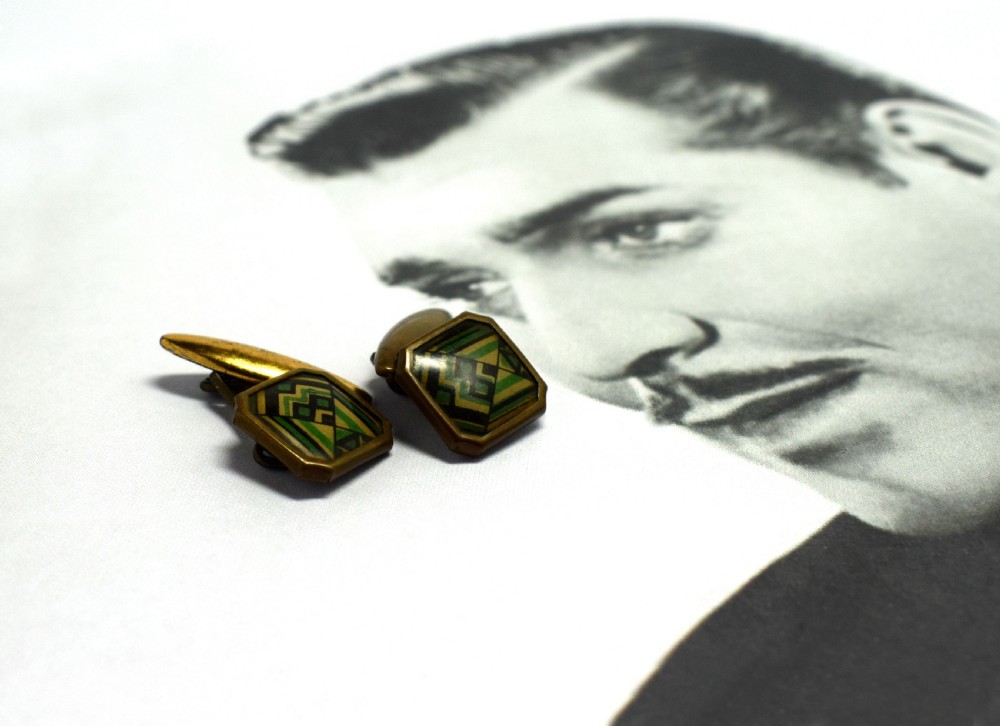 A pair of Art Deco gents cufflinks featuring octagonal faces inlaid with geometric green, black, and yellow enamel patterns framed in brass metal. View VI