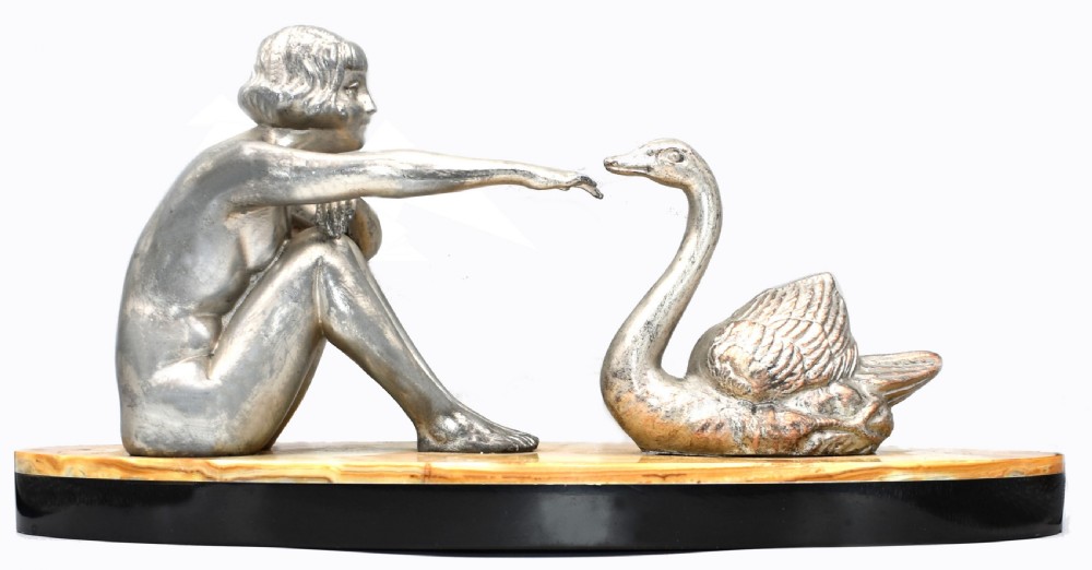 A silvered metal Art Deco sculpture featuring a seated female figure reaching towards a swan, mounted on a two-tone onyx and marble base.