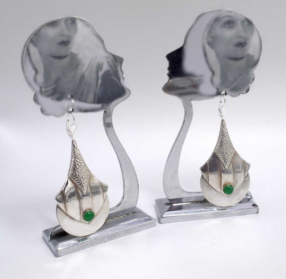 A pair of Art Deco style silver-plated drop earrings featuring geometric fan shapes, hammered detailing, and round green glass cabochons.