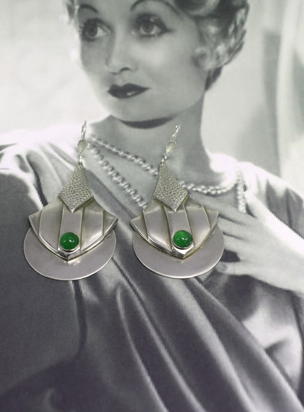 A pair of Art Deco style silver-plated drop earrings featuring geometric fan shapes, hammered detailing, and round green glass cabochons. View VII