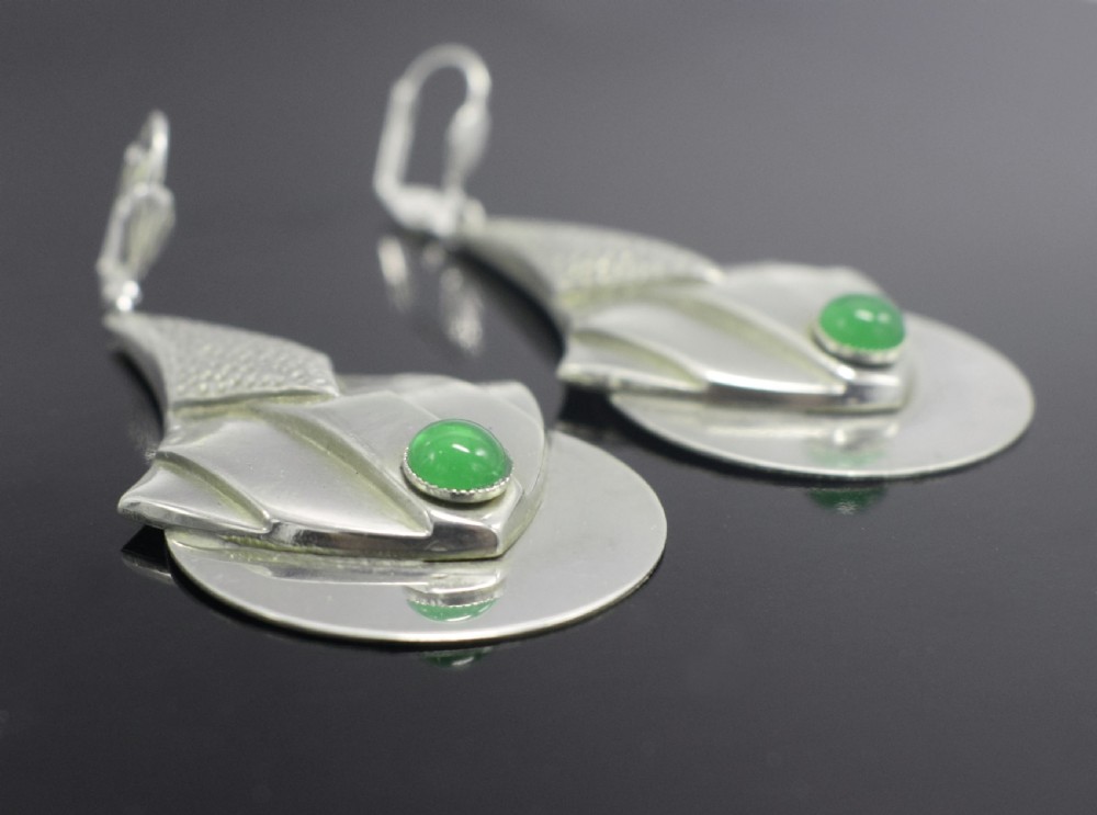 A pair of Art Deco style silver-plated drop earrings featuring geometric fan shapes, hammered detailing, and round green glass cabochons. View IX
