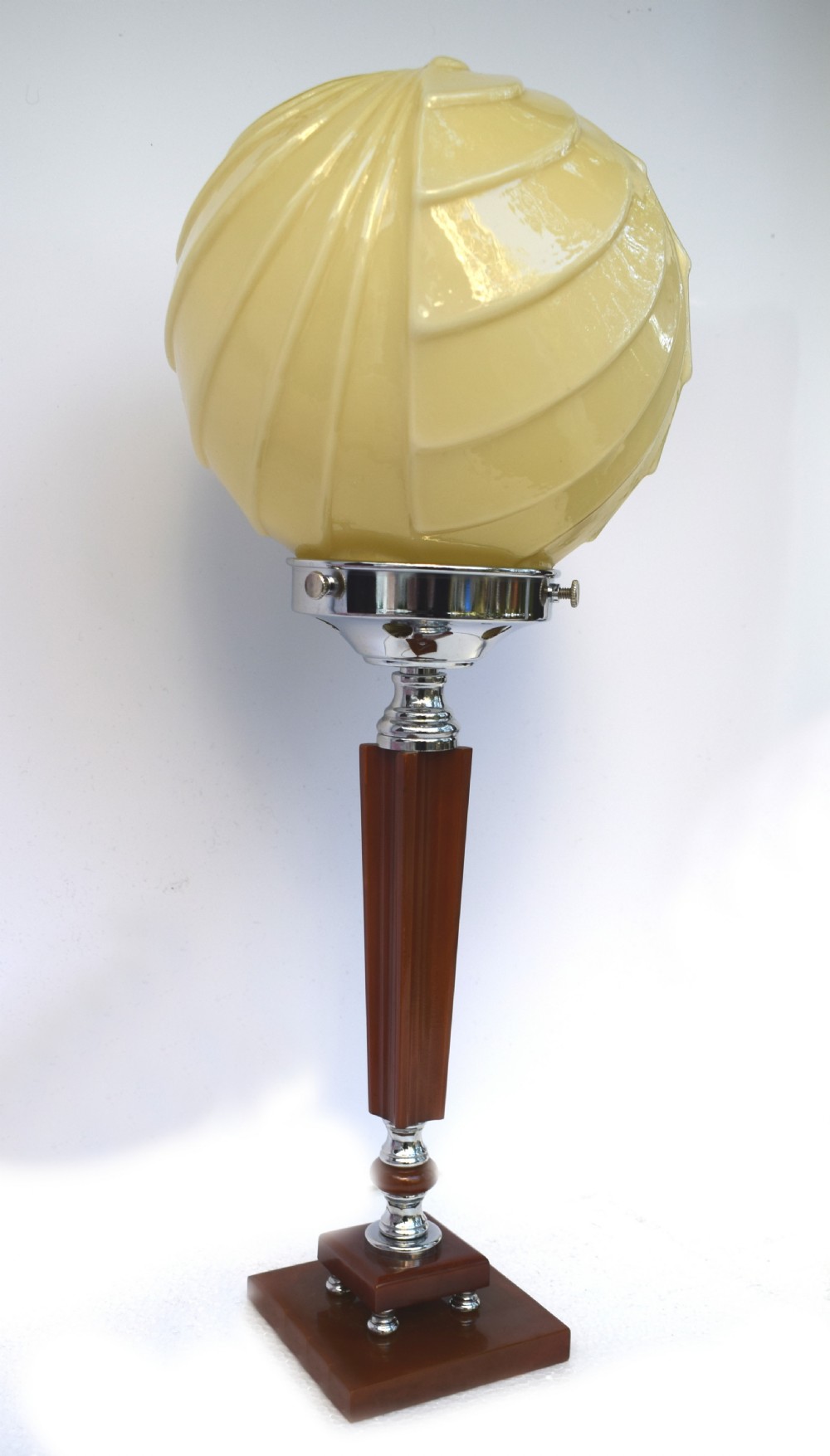 An Art Deco table lamp featuring a cream swirl glass globe shade set on a faceted amber Catalin resin and chrome stem base. View V