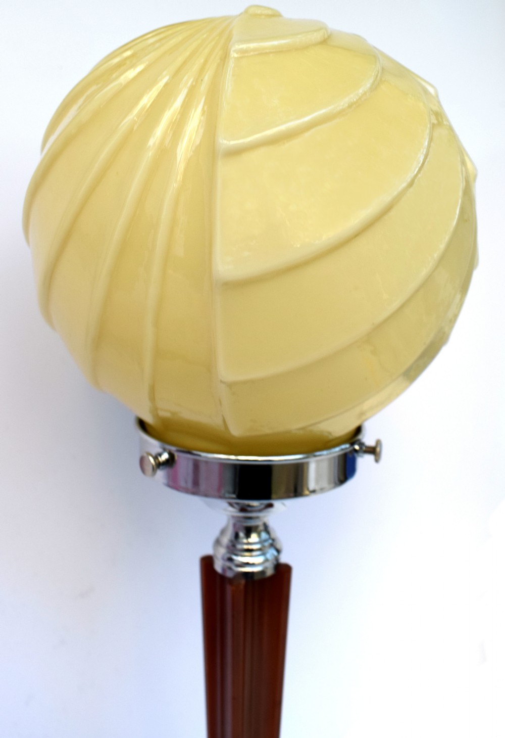 An Art Deco table lamp featuring a cream swirl glass globe shade set on a faceted amber Catalin resin and chrome stem base. View VIII