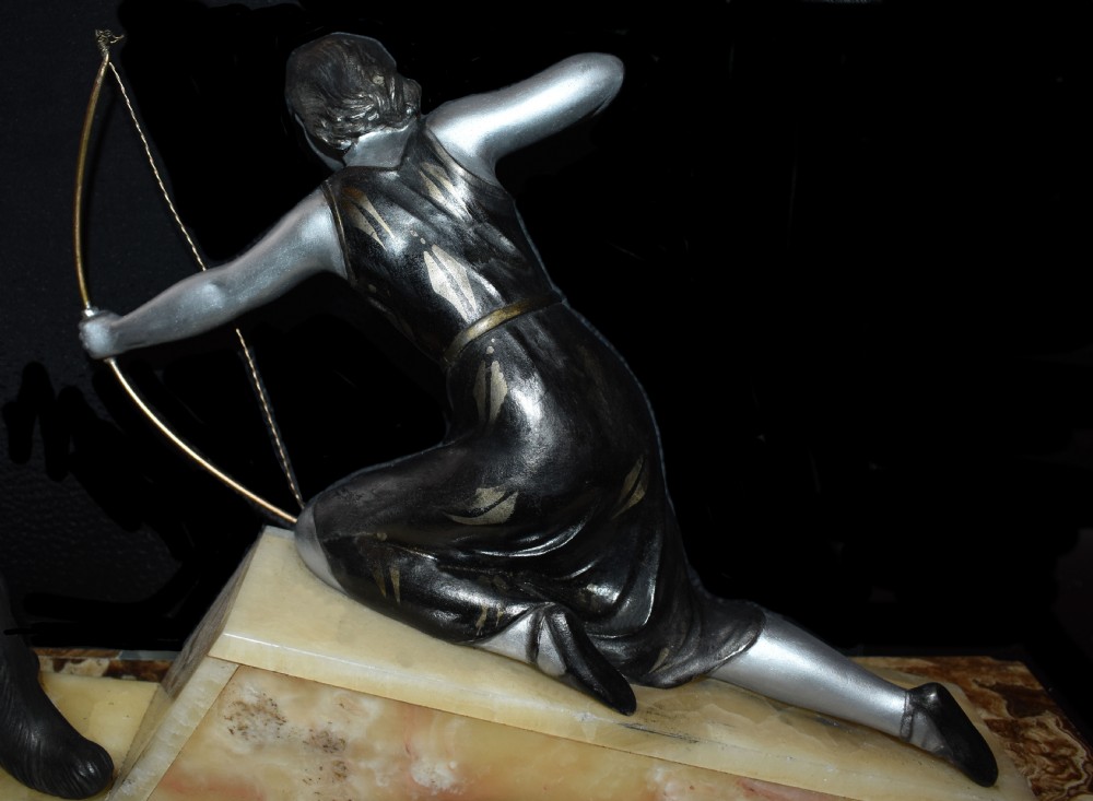 An Art Deco cold-painted metal sculpture depicting a female archer kneeling with a bow alongside a dog on a stepped onyx and marble base. View VIII
