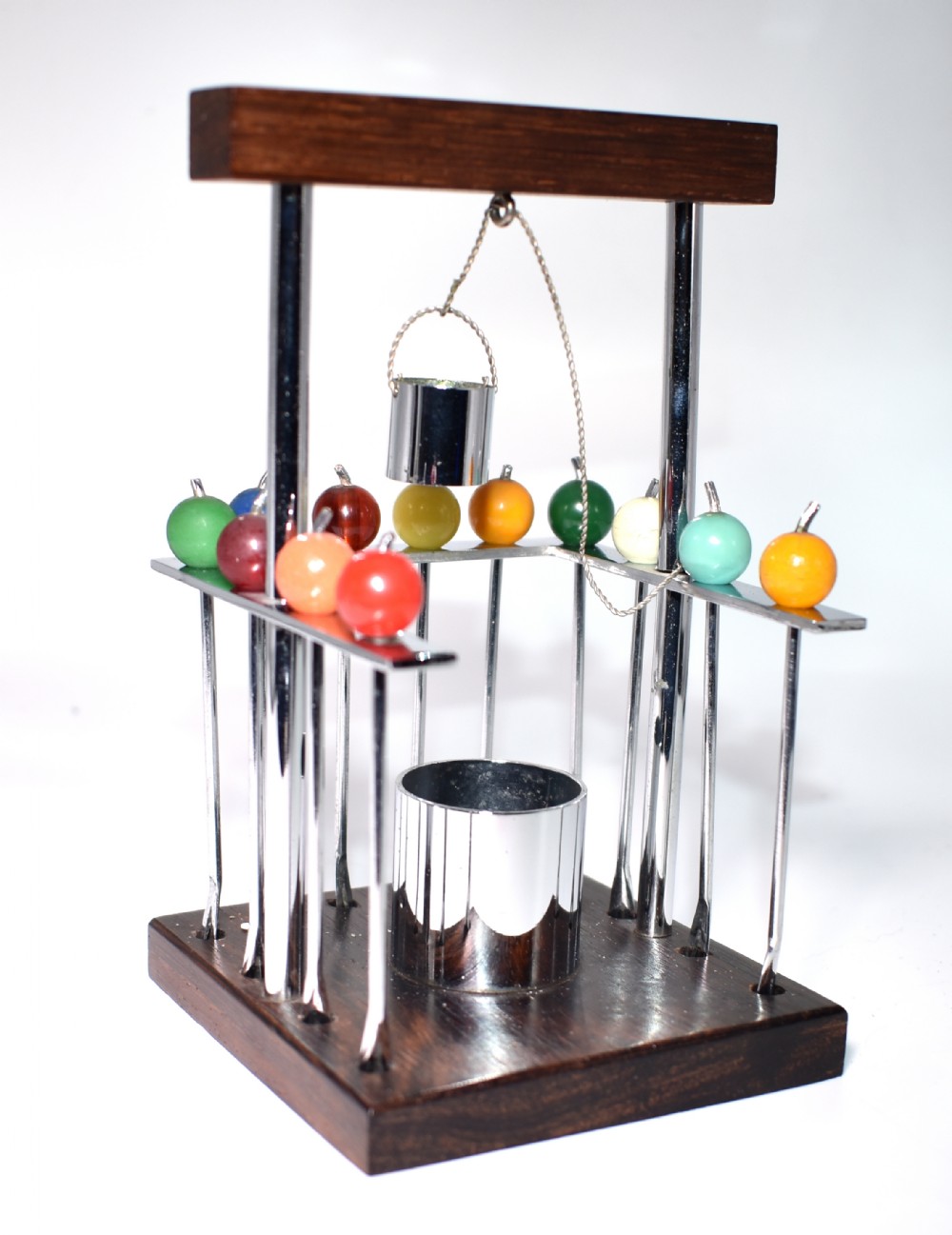 An Art Deco novelty cocktail stick stand shaped as a wishing well with chrome supports, dark wood base, miniature metal bucket, and colourful Bakelite-topped picks.