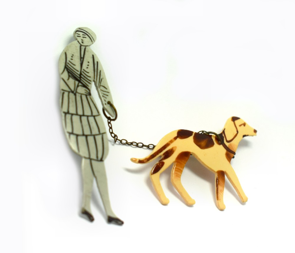 A 1930s Art Deco celluloid novelty brooch depicting a figure walking a spotted dog linked by a small metal chain. View V