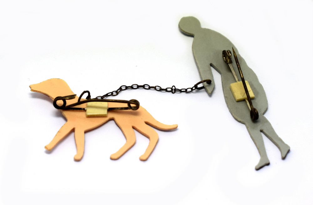 A 1930s Art Deco celluloid novelty brooch depicting a figure walking a spotted dog linked by a small metal chain. View VI