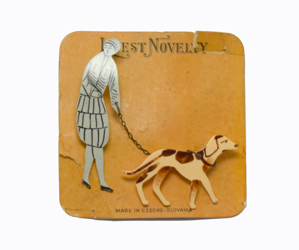 A 1930s Art Deco celluloid novelty brooch depicting a figure walking a spotted dog linked by a small metal chain. View VII