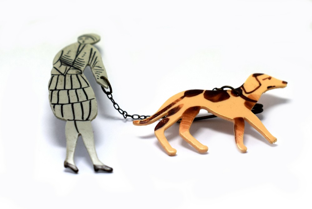 A 1930s Art Deco celluloid novelty brooch depicting a figure walking a spotted dog linked by a small metal chain. View IX