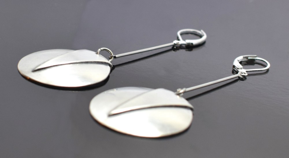 A pair of silver-toned drop earrings featuring circular discs decorated with raised chevron motifs hanging from long linear bars with leverback clasps. View IV