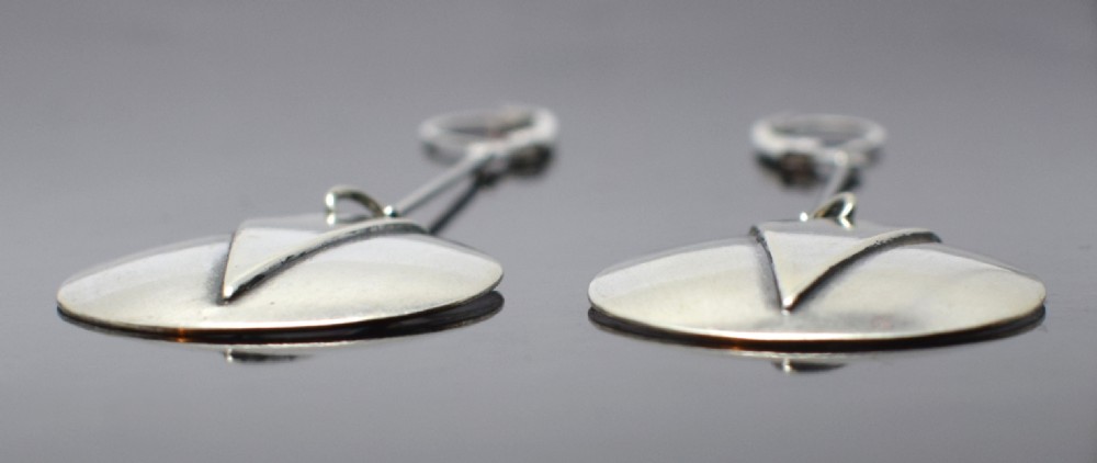 A pair of silver-toned drop earrings featuring circular discs decorated with raised chevron motifs hanging from long linear bars with leverback clasps. View VI