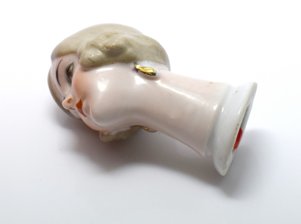 An Art Deco glazed porcelain half doll bust featuring a blonde bob haircut, stylized facial makeup, and a smooth neck base. View X