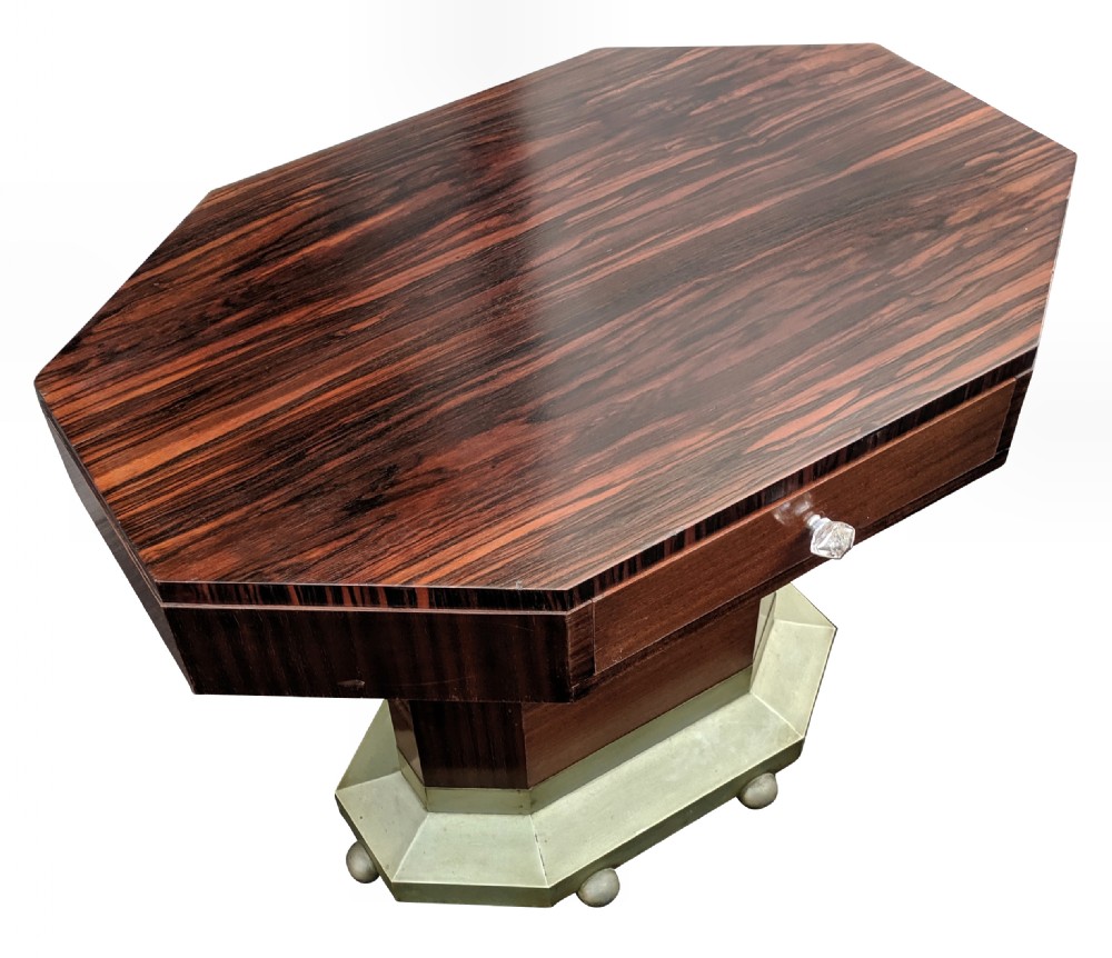 An octagonal Art Deco centre table featuring dark Macassar ebony veneer, a central drawer with a clear glass knob, and a stepped faceted pedestal base. View VI