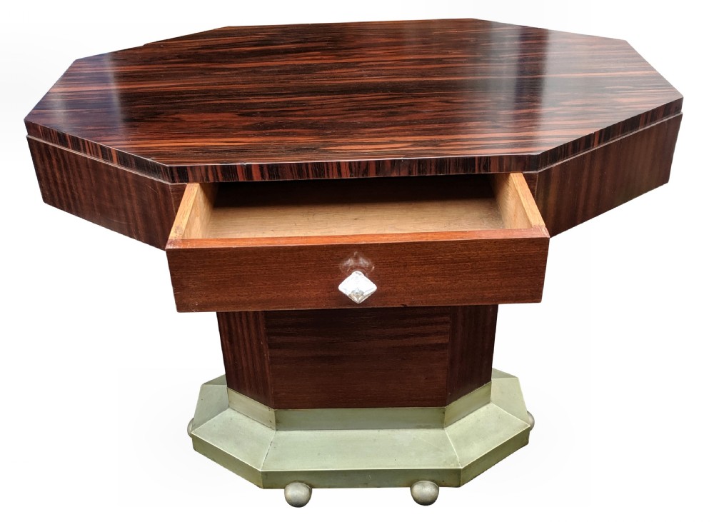 An octagonal Art Deco centre table featuring dark Macassar ebony veneer, a central drawer with a clear glass knob, and a stepped faceted pedestal base. View IX