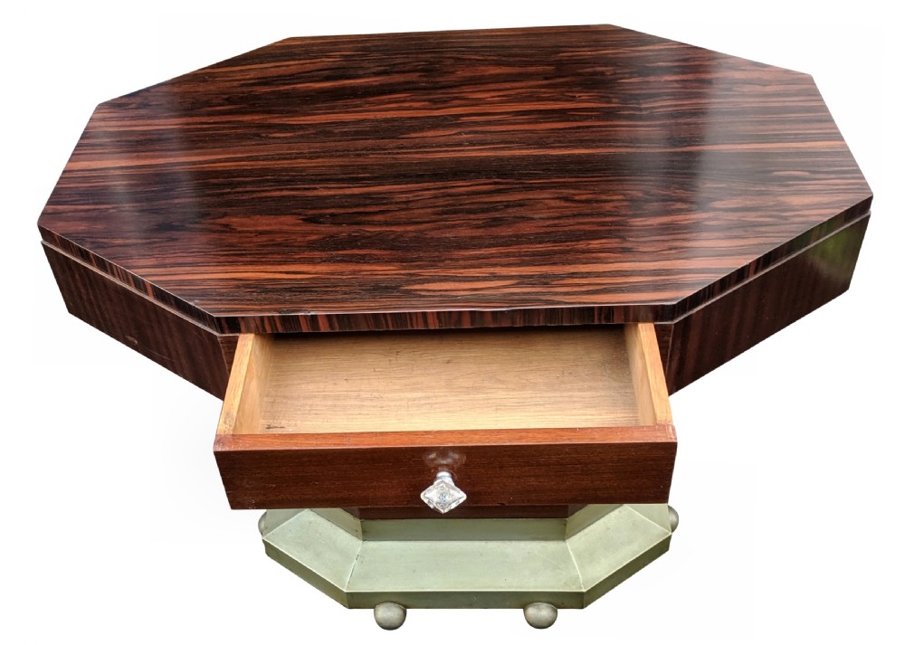An octagonal Art Deco centre table featuring dark Macassar ebony veneer, a central drawer with a clear glass knob, and a stepped faceted pedestal base. View X