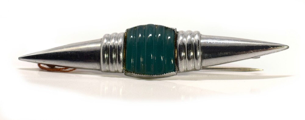 An Art Deco chrome-plated modernist brooch featuring a central ribbed green block flanked by stepped collars and pointed conical ends.