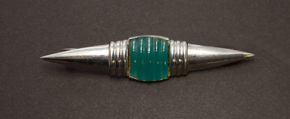 An Art Deco chrome-plated modernist brooch featuring a central ribbed green block flanked by stepped collars and pointed conical ends. View VI