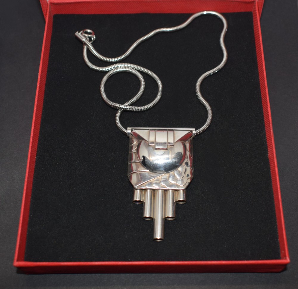 An Art Deco style silver-coloured chrome pendant featuring geometric stepped tubes and a central semicircle motif attached to a snake chain. View II