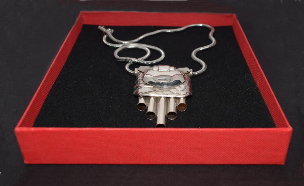 An Art Deco style silver-coloured chrome pendant featuring geometric stepped tubes and a central semicircle motif attached to a snake chain. View III