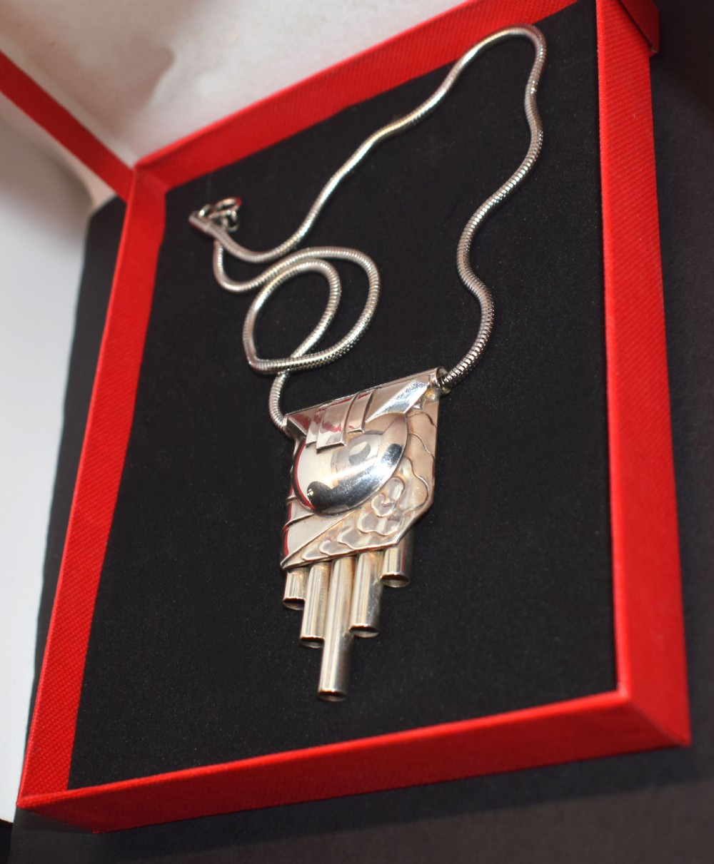 An Art Deco style silver-coloured chrome pendant featuring geometric stepped tubes and a central semicircle motif attached to a snake chain. View IV