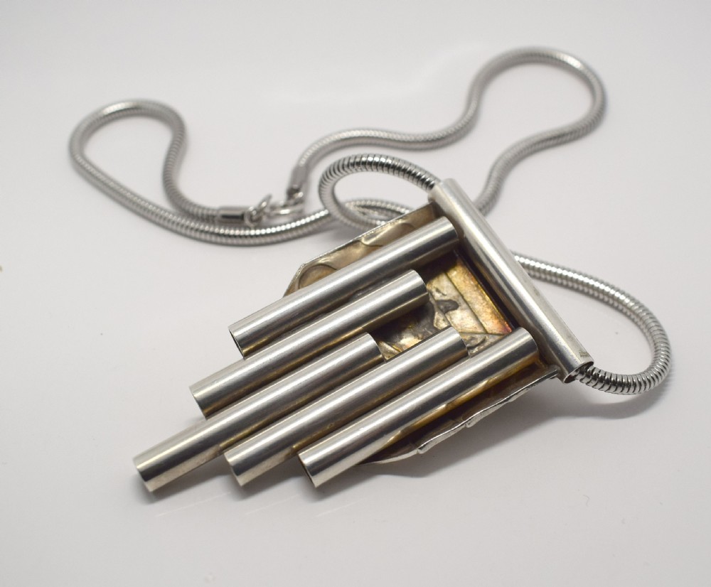 An Art Deco style silver-coloured chrome pendant featuring geometric stepped tubes and a central semicircle motif attached to a snake chain. View VI