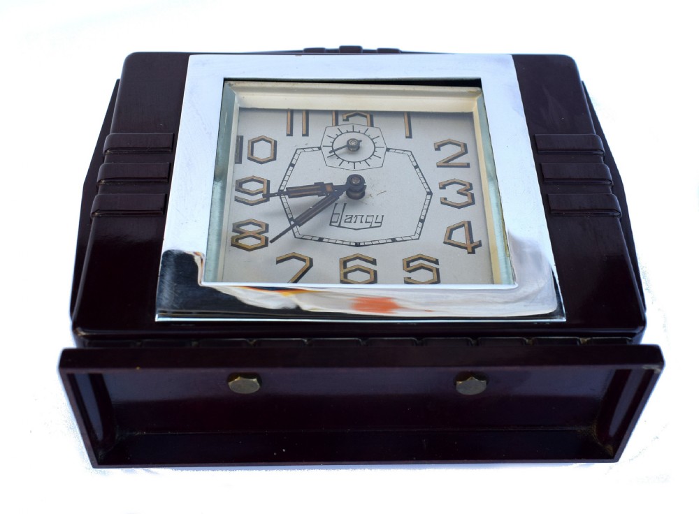 A square dark brown Bakelite mantel clock featuring stepped side details, a polished chrome inner frame, and a cream dial with Art Deco numeric typography. View IV