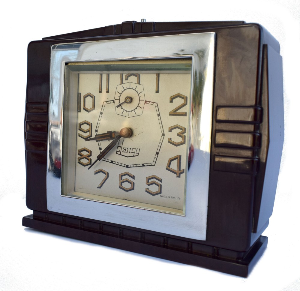 A square dark brown Bakelite mantel clock featuring stepped side details, a polished chrome inner frame, and a cream dial with Art Deco numeric typography. View V