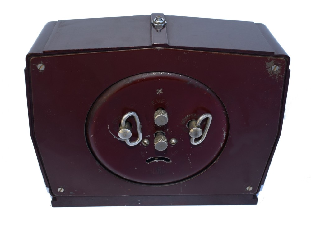 A square dark brown Bakelite mantel clock featuring stepped side details, a polished chrome inner frame, and a cream dial with Art Deco numeric typography. View VI
