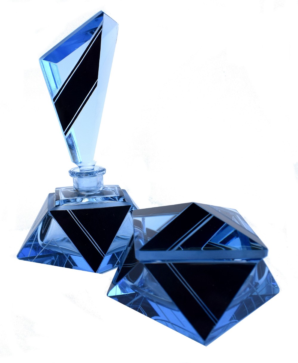 An Art Deco light blue glass vanity set consisting of a geometric scent bottle with a tall stopper and a matching powder box decorated with black triangular detailing.