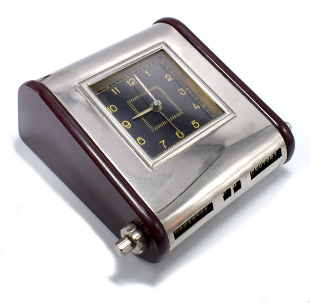 An Art Deco Hungarian desk clock featuring burgundy Bakelite side panels, a polished chrome casing, a square black dial, and integrated day and month calendar displays.