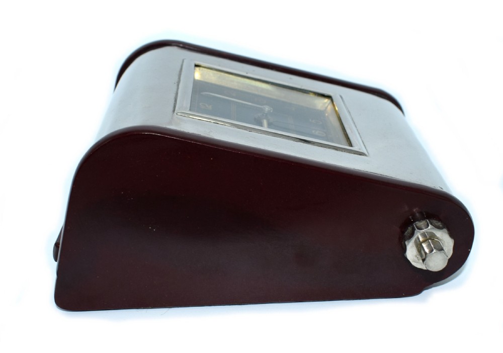 An Art Deco Hungarian desk clock featuring burgundy Bakelite side panels, a polished chrome casing, a square black dial, and integrated day and month calendar displays. View III