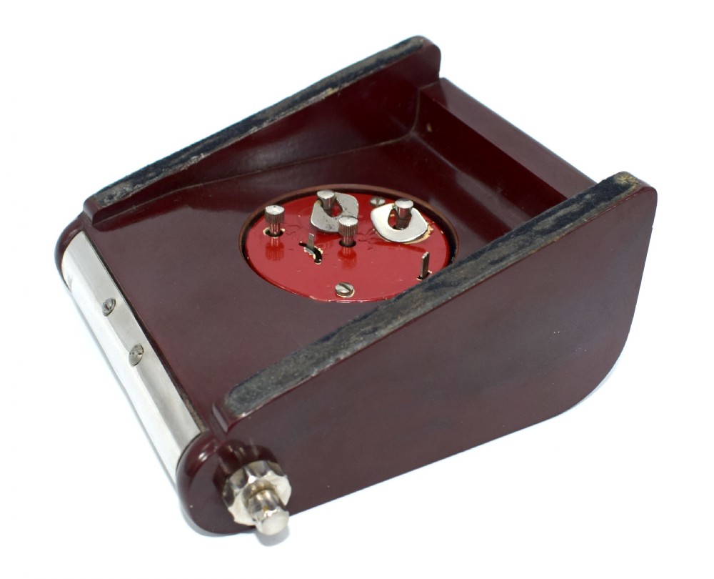 An Art Deco Hungarian desk clock featuring burgundy Bakelite side panels, a polished chrome casing, a square black dial, and integrated day and month calendar displays. View VII
