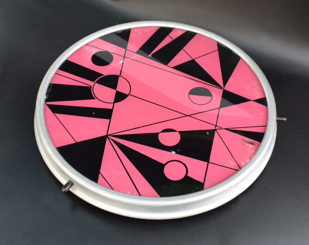 A circular Art Deco Lazy Susan featuring a pink and black abstract geometric pattern encased within a silver metal rim.