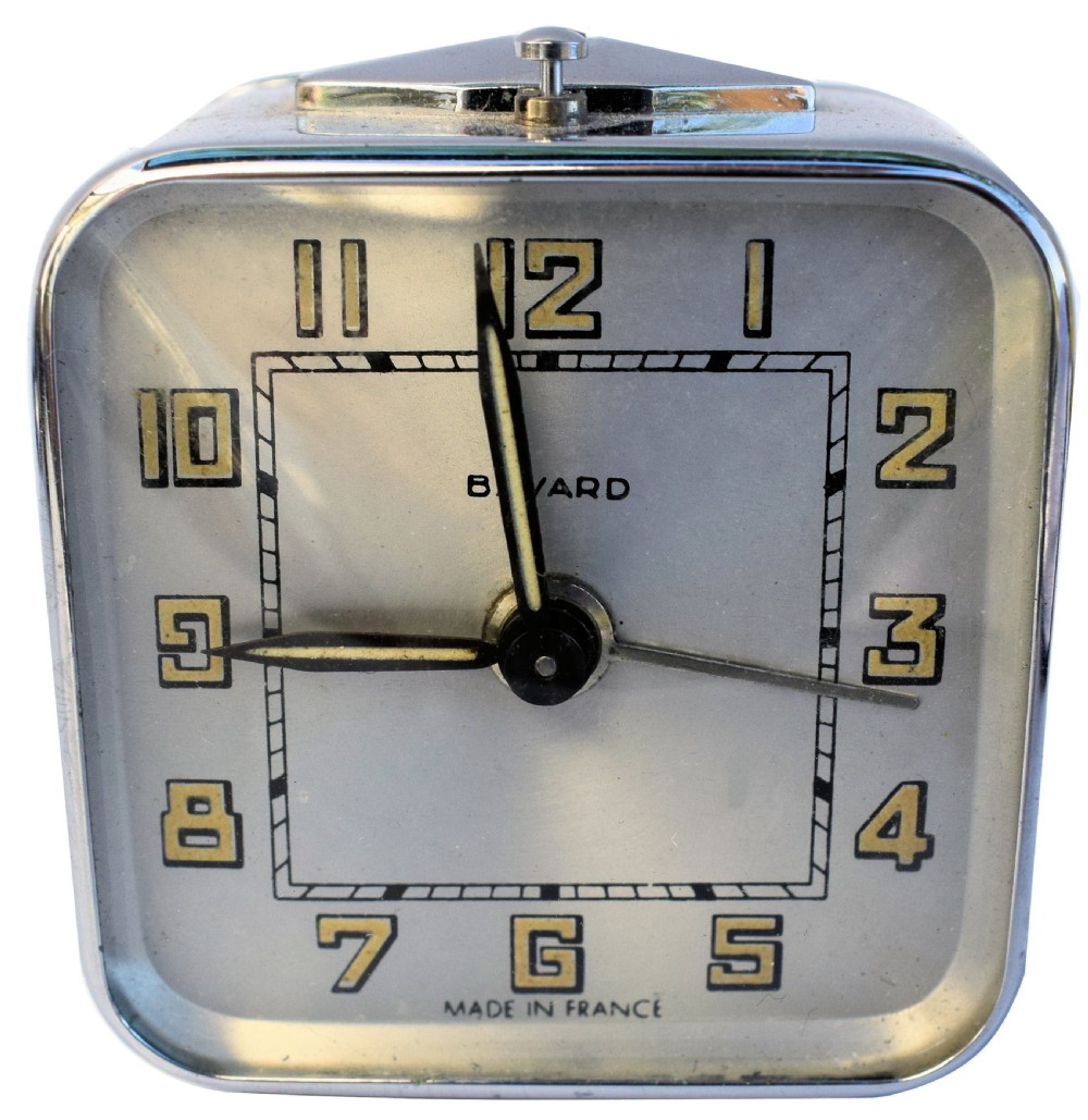A square French Art Deco chrome alarm clock with stylized yellow numerals, a silver dial, and a top shut-off button.
