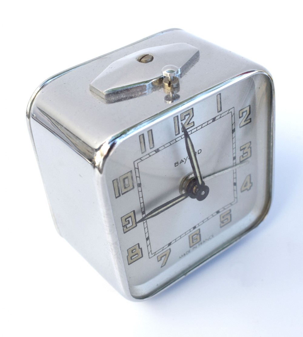 A square French Art Deco chrome alarm clock with stylized yellow numerals, a silver dial, and a top shut-off button. View V