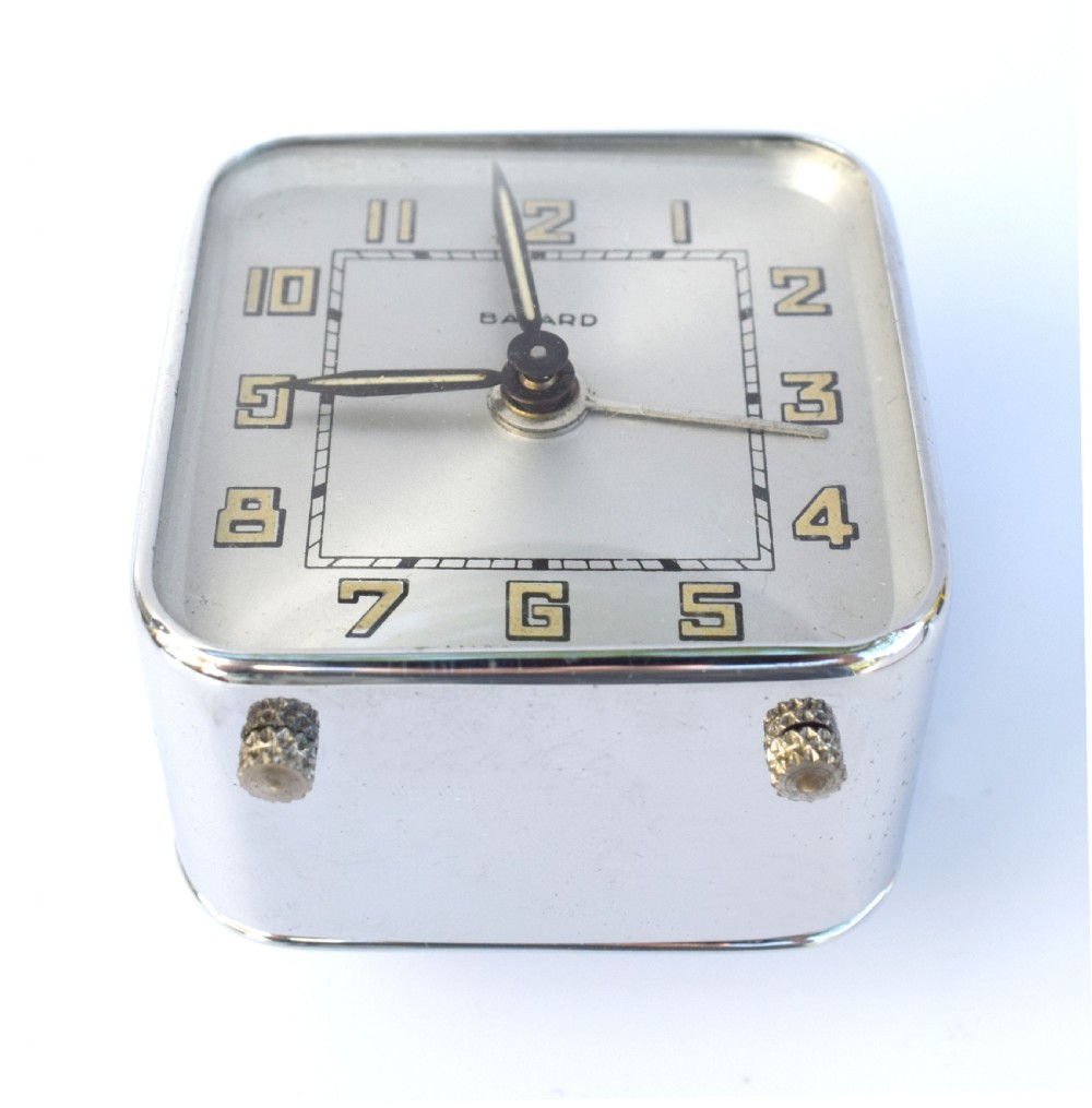 A square French Art Deco chrome alarm clock with stylized yellow numerals, a silver dial, and a top shut-off button. View VI