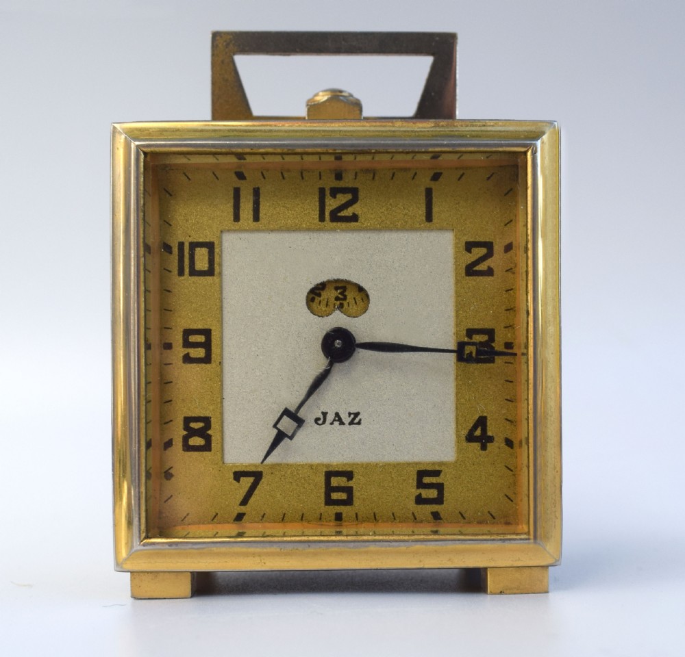 A square French Art Deco miniature alarm clock with a gilded brass casing and two-tone cream dial. View VI