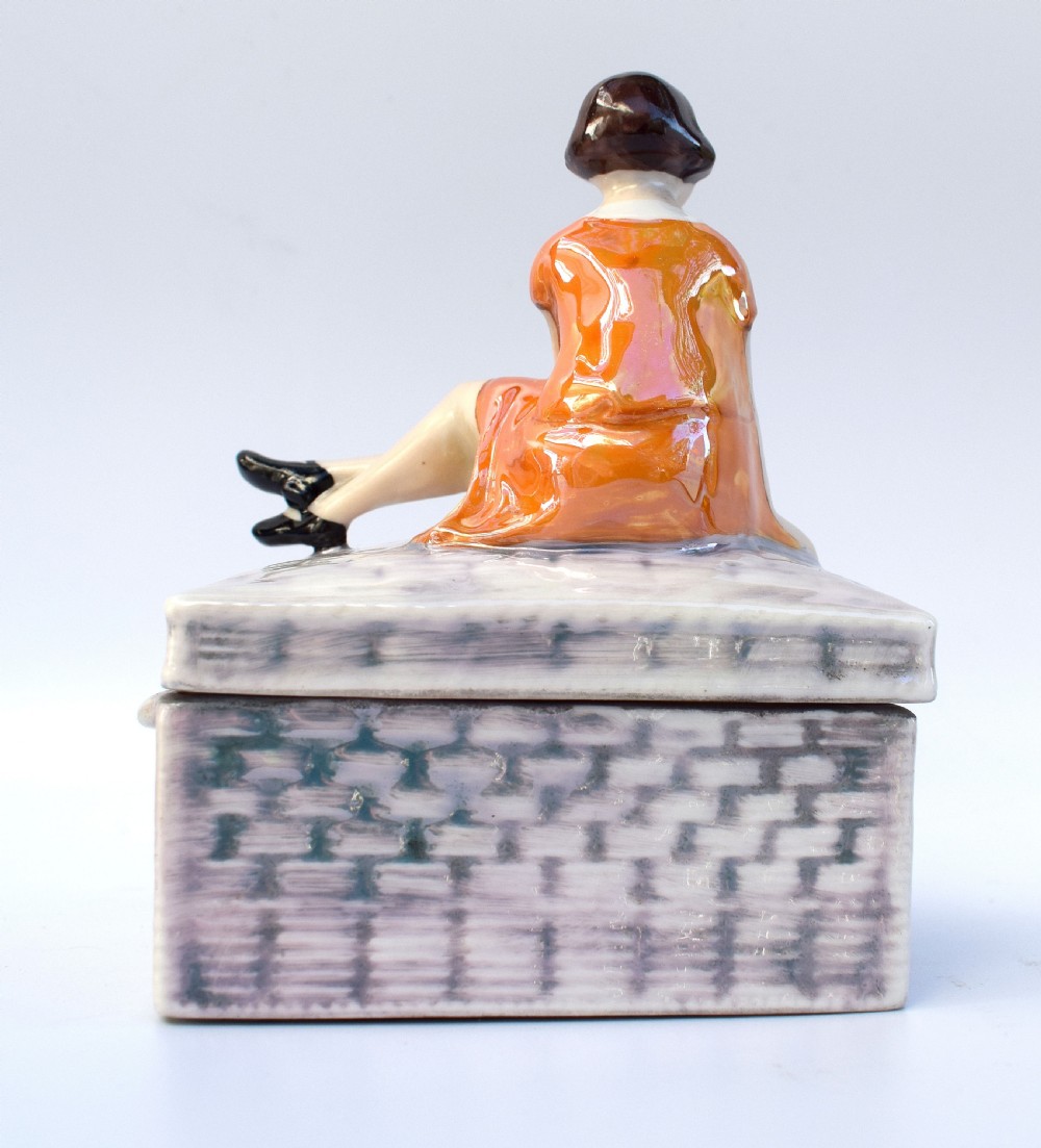 A glazed ceramic Art Deco trinket box featuring a lid adorned with a figurine of a seated girl in an orange dress with a puppy, over a basketweave patterned base. View VII