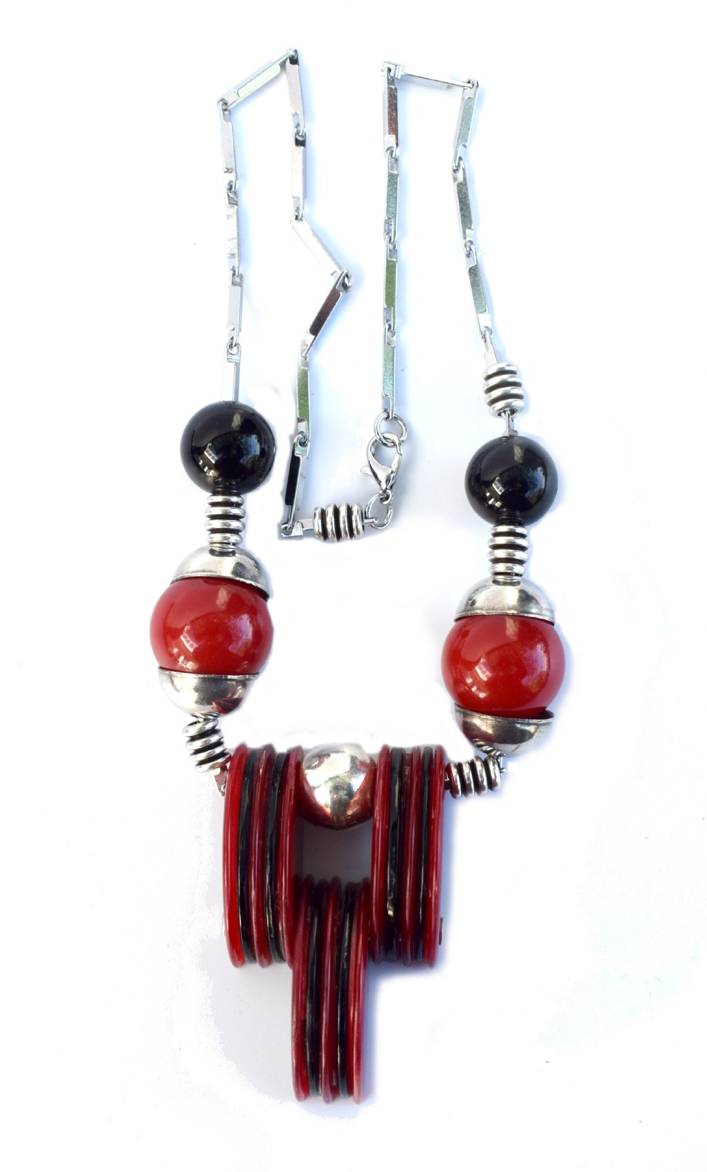 An Art Deco modernist necklace featuring red and black spherical beads, coiled silver-toned metal spacers, and a geometric central pendant composed of stacked red and black discs on a metal link chain.