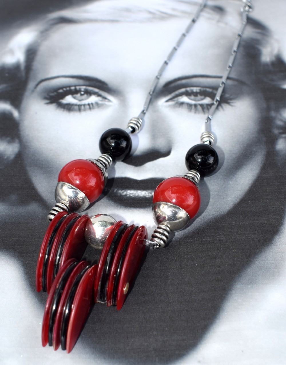 An Art Deco modernist necklace featuring red and black spherical beads, coiled silver-toned metal spacers, and a geometric central pendant composed of stacked red and black discs on a metal link chain. View III
